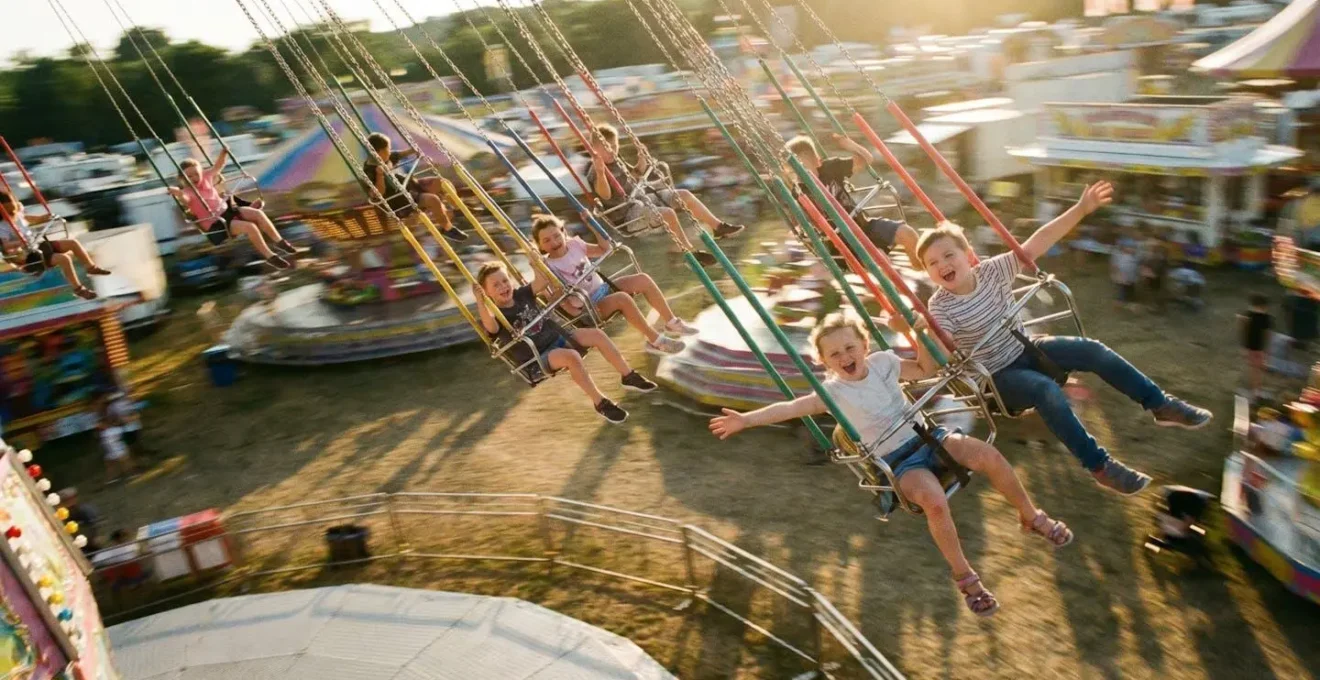 Vue plongeante sur des enfants en train de tourner sur un carrousel à chaises volantes, nacelles en mouvement, rires et bras tendus